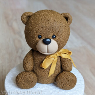 Handmade brown fondant teddy bear cake topper with textured fur and metallic gold bow