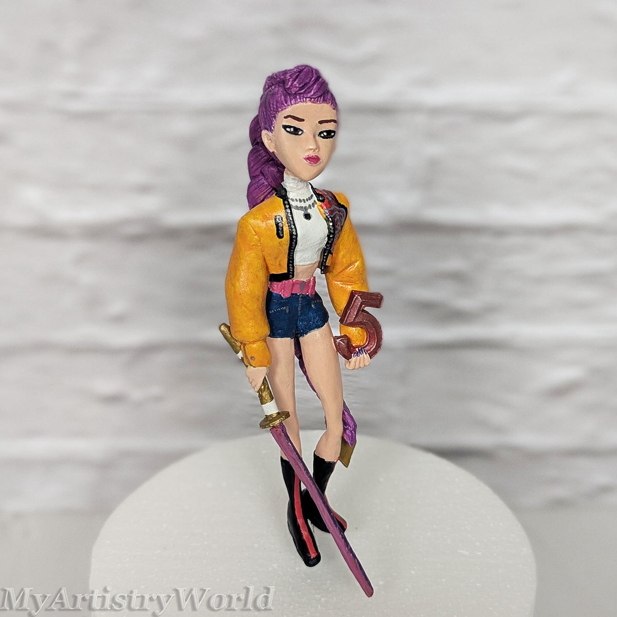 Side view of a handmade Rumi clay cake topper with sword.