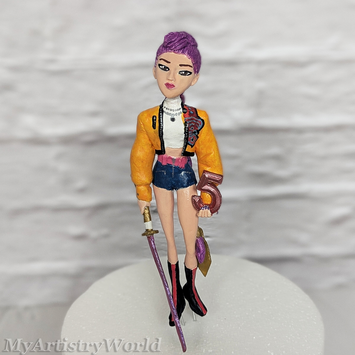 Clay custom Rumi cake topper inspired by KPop Demon Hunters, sculpted from clay with purple hair, yellow jacket, sword, and personalized number